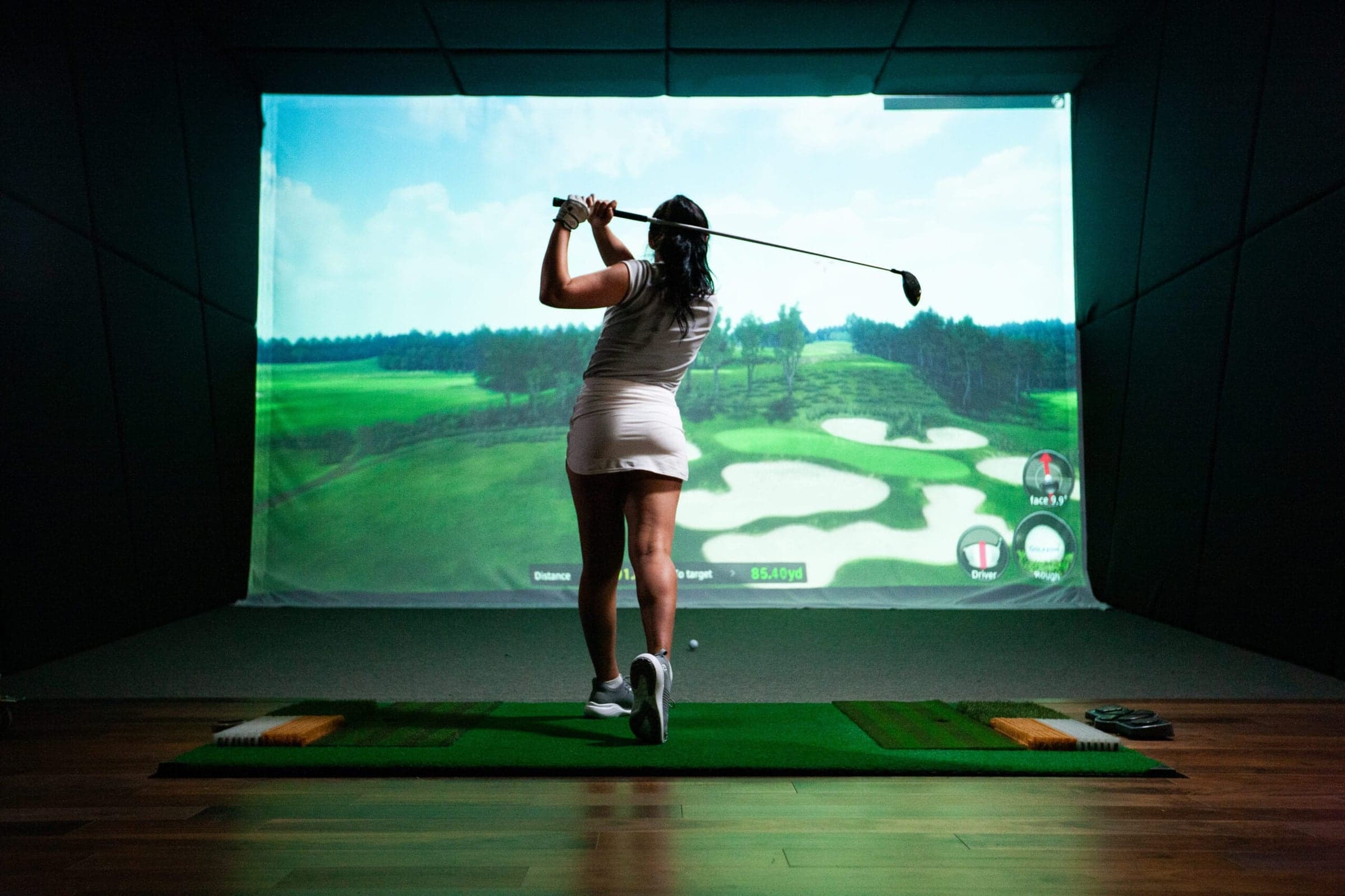9Yards Golf Course Simulators & Lounge of Washington, PA — Golfer at the top of the backswing in a GOLFZON bay, warm timber floor, projected parkland