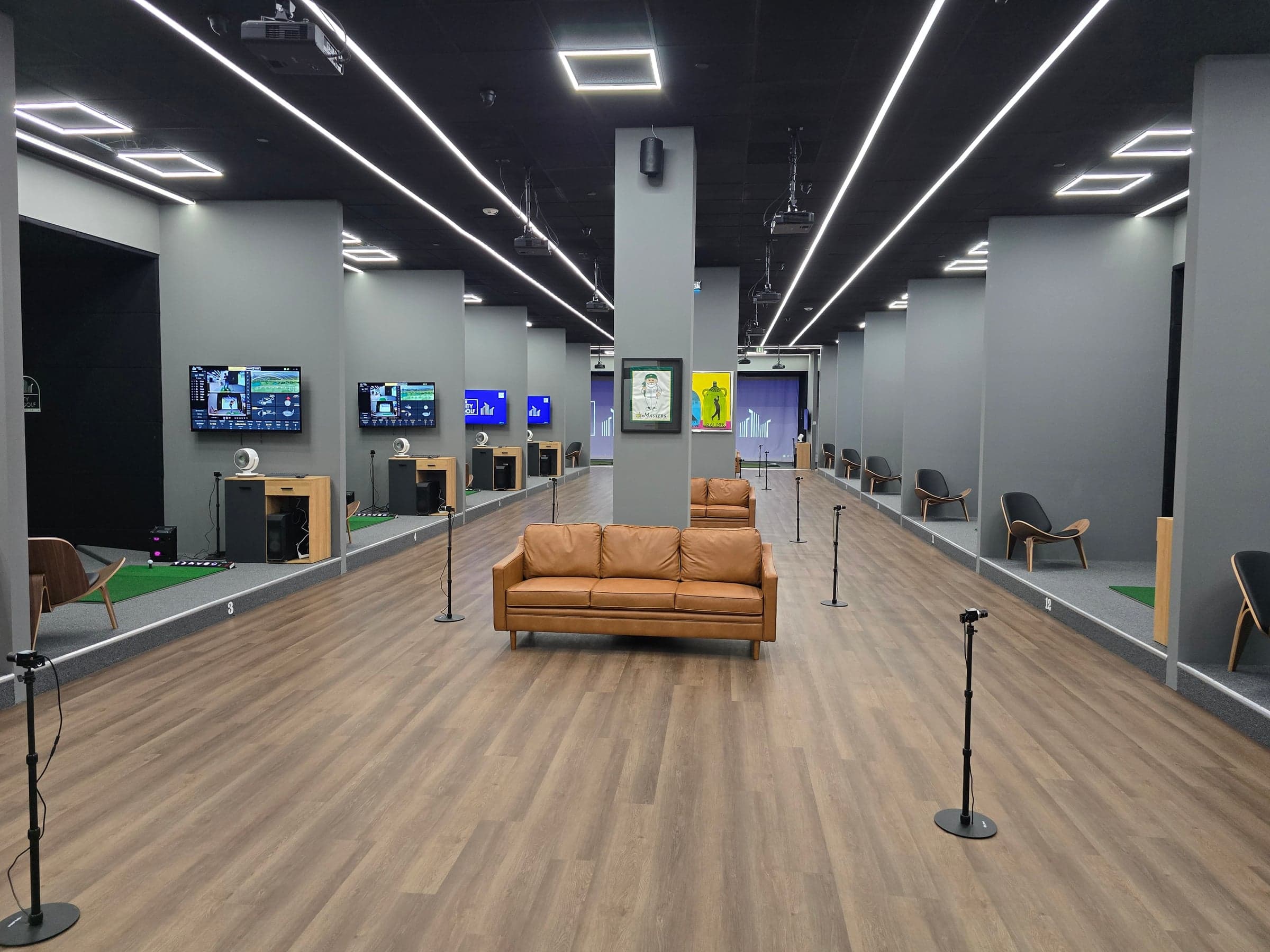 The City Golf — Wide view down the range room: linear LED ceiling strips, bay row with monitors, tan leath