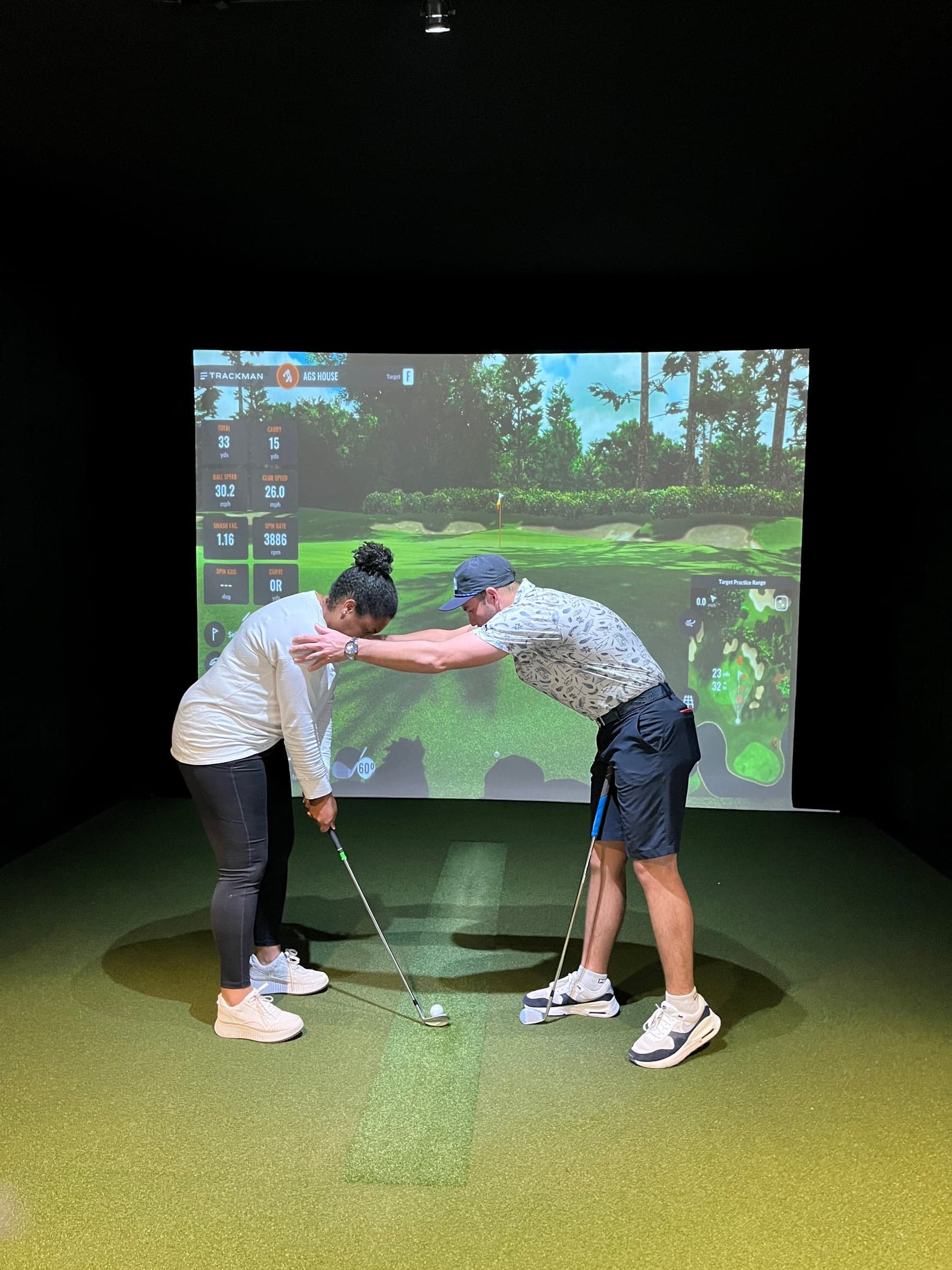Atlanta Golf & Social | Chamblee — A lesson in progress: instructor adjusting a student's setup on the mat, TrackMan data ove